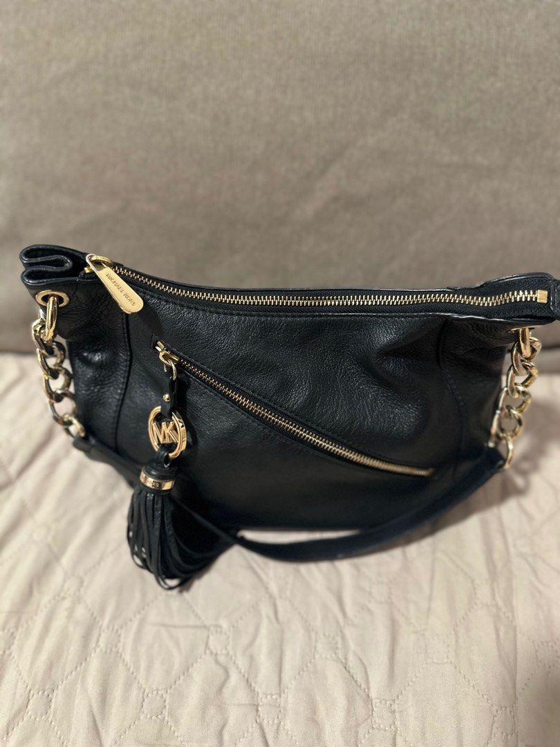 Michael Kors Black Leather Hobo Bag (Category: Luxury Bags & Wallets) located in Mandaluyong City. Submitted by grace.dt (Listing ID 1403836574, Image 3). Description: Black leather hobo bag from Michael Kors. Features a gold-tone chain strap and zipper details. Includes a tassel and the MK logo charm. The interior is lined with the Michael Kors logo. The bag has a zipper closure and a shoulder strap. The hardware is gold-toned..