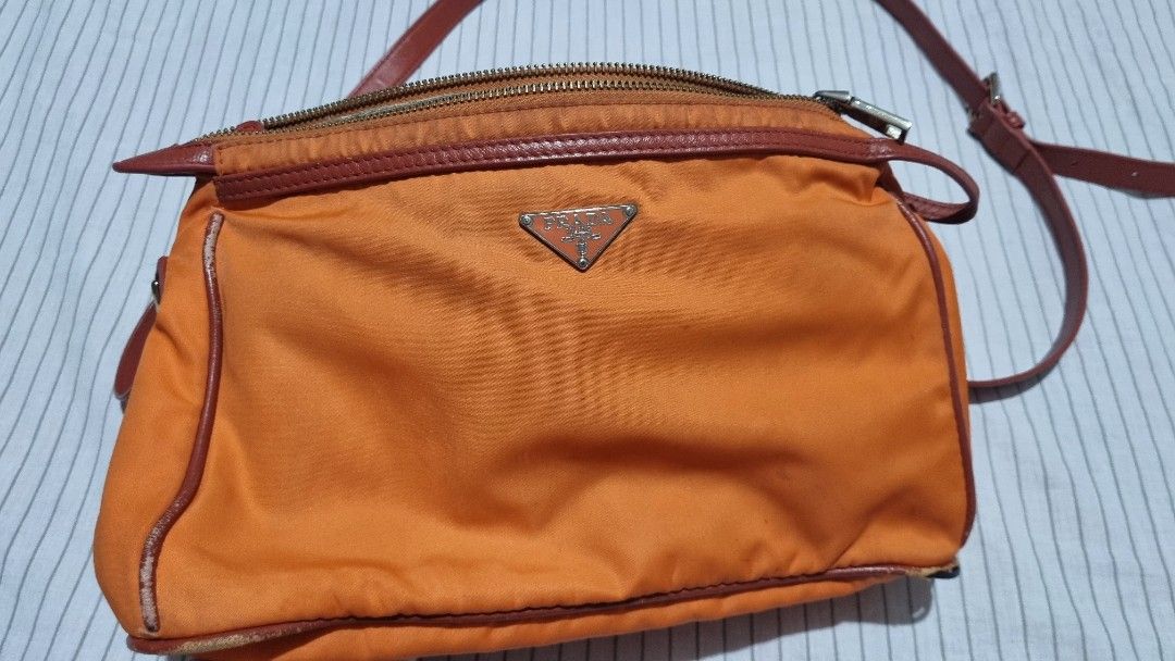 Prada Orange Crossbody Bag (Category: Luxury Bags & Wallets) located in Davao. Submitted by noona.nette (Listing ID 1403873874, Image 2). Description: 💯Authentic -Personal preloved - Orange crossbody bag - Top zipper closure - Prada logo on front - Detachable shoulder strap - Patterned interior lining - Shows wear on corners and edges.