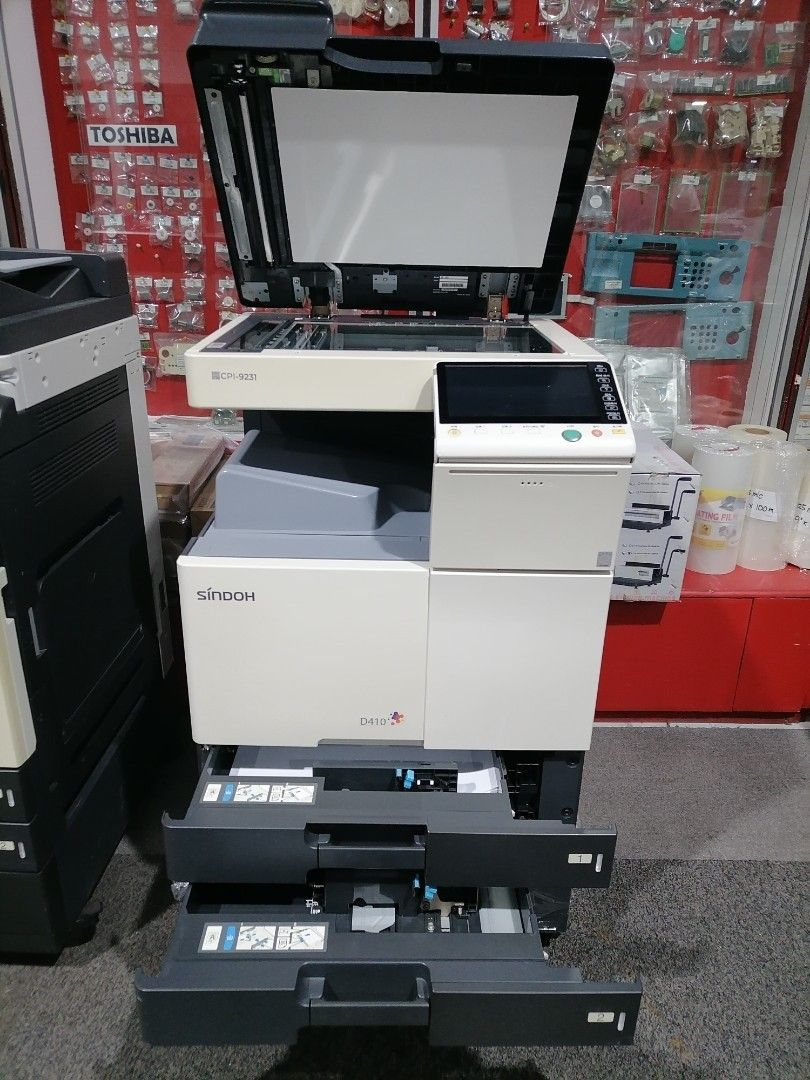 Sindoh D410 Photocopier (Category: Printers, Scanners & Copiers) located in Quezon City. Submitted by copieronlineinc (Listing ID 1403879854, Image 2). Description: Sindoh D410 photocopier is on Early Year End Sale. Features a control panel with a green button. Includes two paper trays. The model number is visible on the front. The unit is white and gray in color. The photocopier is wrapped in plastic..