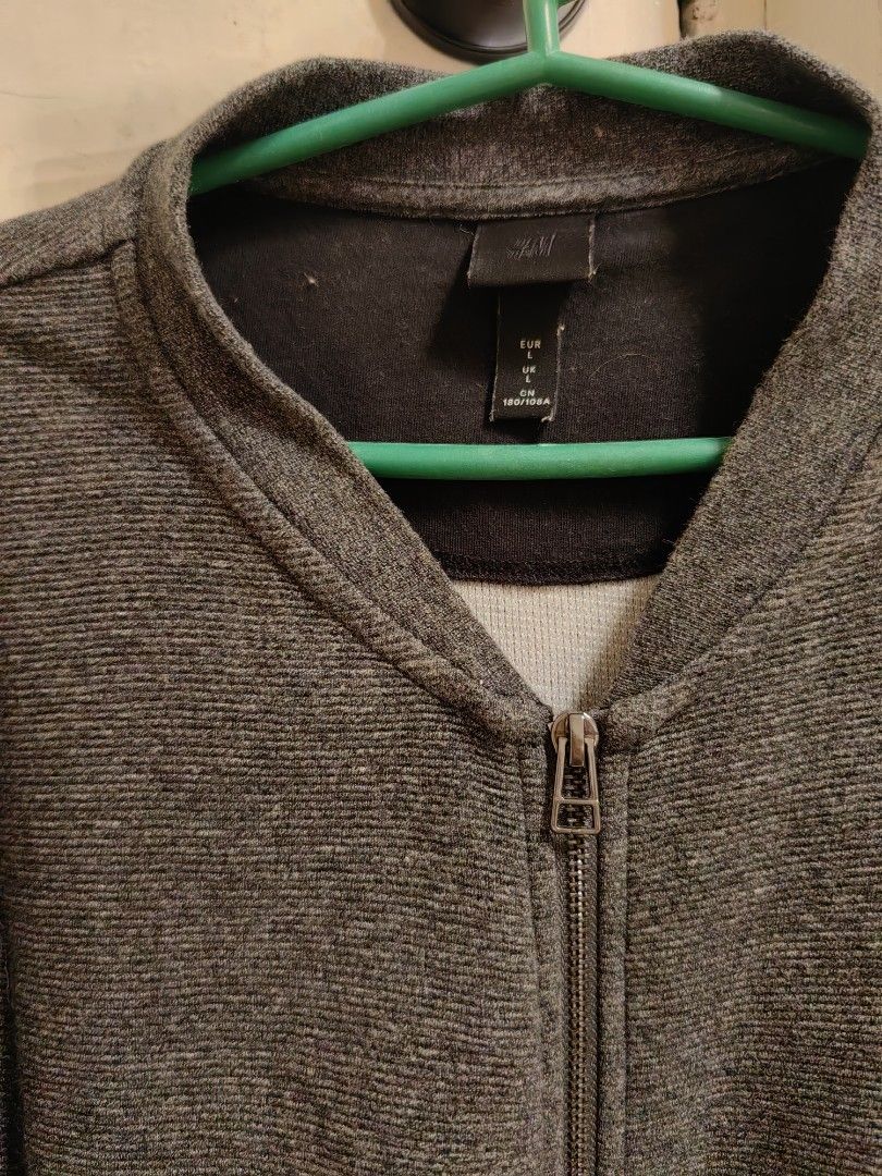 H&M Gray Zip-Up Jacket (Category: Coats, Jackets and Outerwear) located in Cavite. Submitted by klosetnijuan (Listing ID 1404267872, Image 3). Description: H&M jacket features a full zip closure and two front pockets. It has a ribbed texture and a stand-up collar. The jacket is a dark gray color. The size tag indicates it is a size L. The jacket is suitable for casual wear..