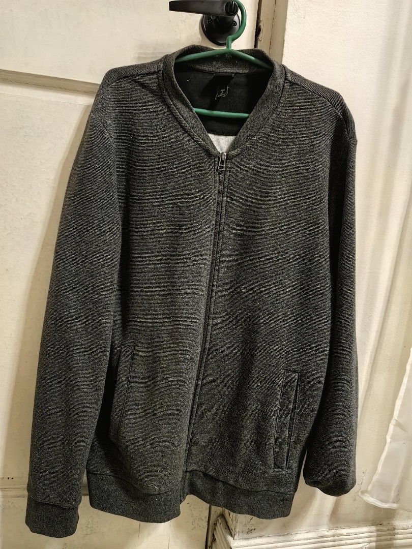 H&M Gray Zip-Up Jacket (Category: Coats, Jackets and Outerwear) located in Cavite. Submitted by klosetnijuan (Listing ID 1404267872, Image 1). Description: H&M jacket features a full zip closure and two front pockets. It has a ribbed texture and a stand-up collar. The jacket is a dark gray color. The size tag indicates it is a size L. The jacket is suitable for casual wear..