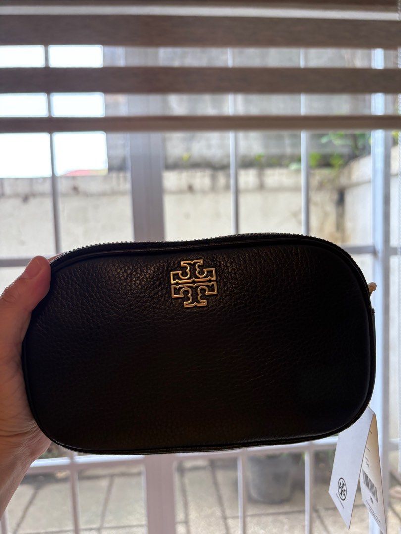 Tory Burch Britten Camera Bag (Category: Luxury Bags & Wallets) located in Cavite. Submitted by louiessaliviac (Listing ID 1404240264, Image 3). Description: The image shows a Tory Burch Britten Camera Bagin black pebbled leather with gold-tone hardware. * The bag features an oval shape and the signature Tory Burch double-T logo on the front. * It has a double-compartment design with one interior slip pocket. * The strap is adjustable, allowing i