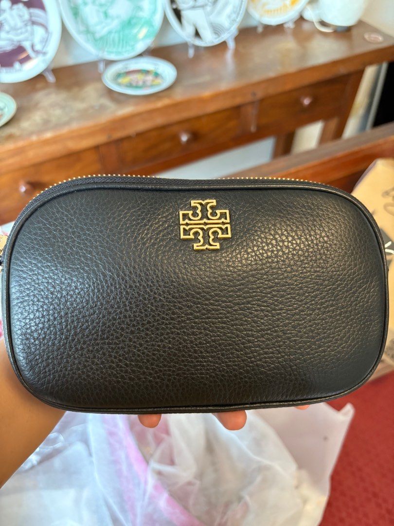 Tory Burch Britten Camera Bag (Category: Luxury Bags & Wallets) located in Cavite. Submitted by louiessaliviac (Listing ID 1404240264, Image 2). Description: The image shows a Tory Burch Britten Camera Bagin black pebbled leather with gold-tone hardware. * The bag features an oval shape and the signature Tory Burch double-T logo on the front. * It has a double-compartment design with one interior slip pocket. * The strap is adjustable, allowing i