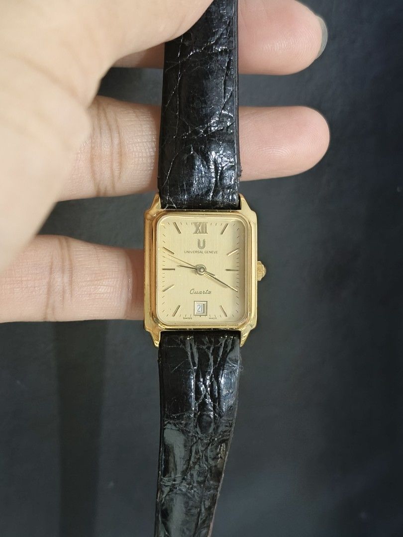 Universal Geneve Quartz Watch (Category: Luxury Watches) located in Taguig. Submitted by mercyeugen28914 (Listing ID 1404314483, Image 2). Description: Elegant Universal Geneve quartz watch with a rectangular gold-toned face. Features a black leather strap with a buckle closure. The watch face displays Roman numerals and a date window. The back of the watch is stainless steel. The strap is embossed with the brand name..