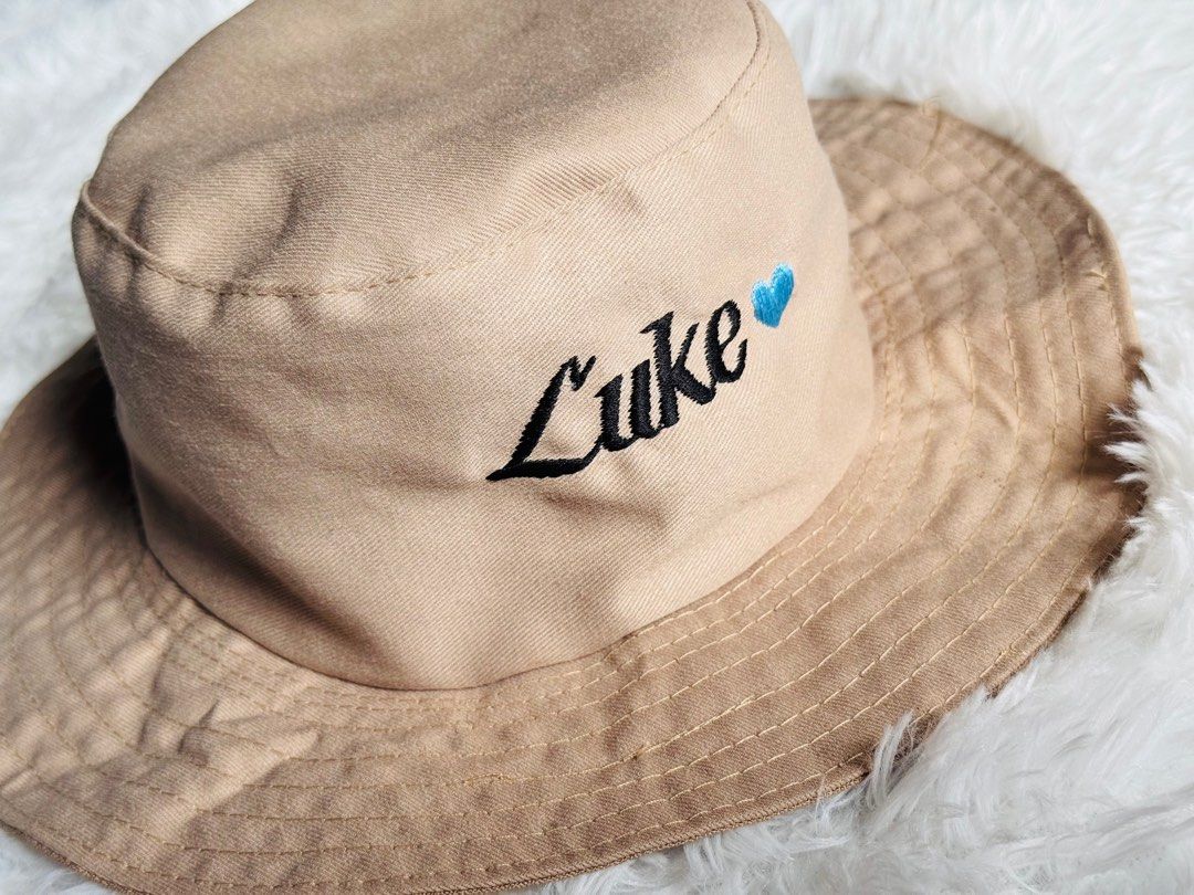Customize Embroidered Bucket Hat with NAME (Category: Babies & Kids Fashion) located in Manila. Submitted by rmdthreads (Listing ID 1404403796, Image 1). Description: - Tan bucket hat - Embroidered with "Luke" and a blue heart - Wide brim - Drawstring included - Perfect for gifts or personal style.