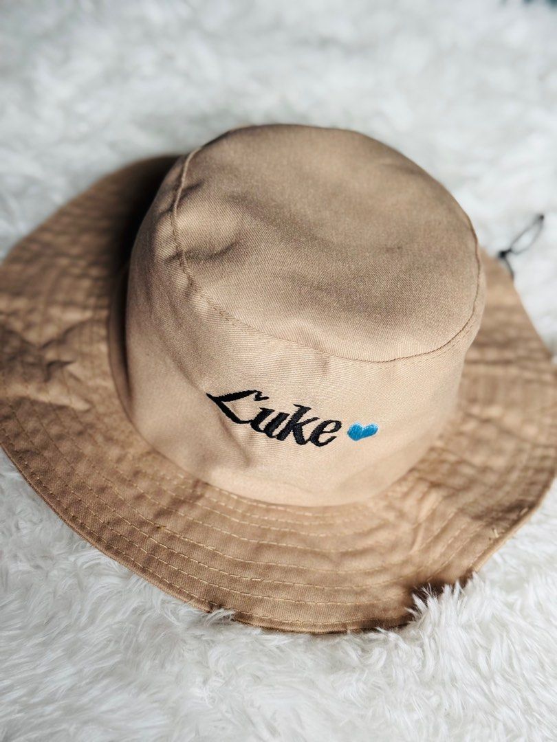 Customize Embroidered Bucket Hat with NAME (Category: Babies & Kids Fashion) located in Manila. Submitted by rmdthreads (Listing ID 1404403796, Image 2). Description: - Tan bucket hat - Embroidered with "Luke" and a blue heart - Wide brim - Drawstring included - Perfect for gifts or personal style.