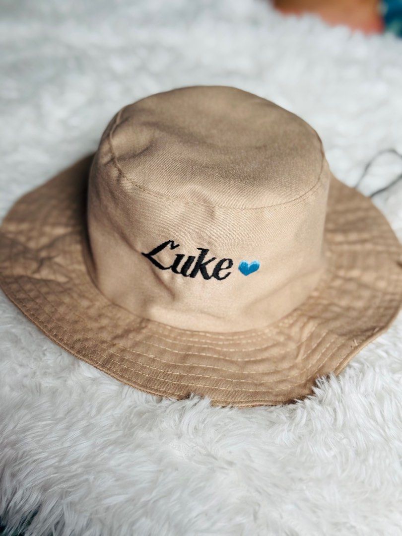 Customize Embroidered Bucket Hat with NAME (Category: Babies & Kids Fashion) located in Manila. Submitted by rmdthreads (Listing ID 1404403796, Image 3). Description: - Tan bucket hat - Embroidered with "Luke" and a blue heart - Wide brim - Drawstring included - Perfect for gifts or personal style.