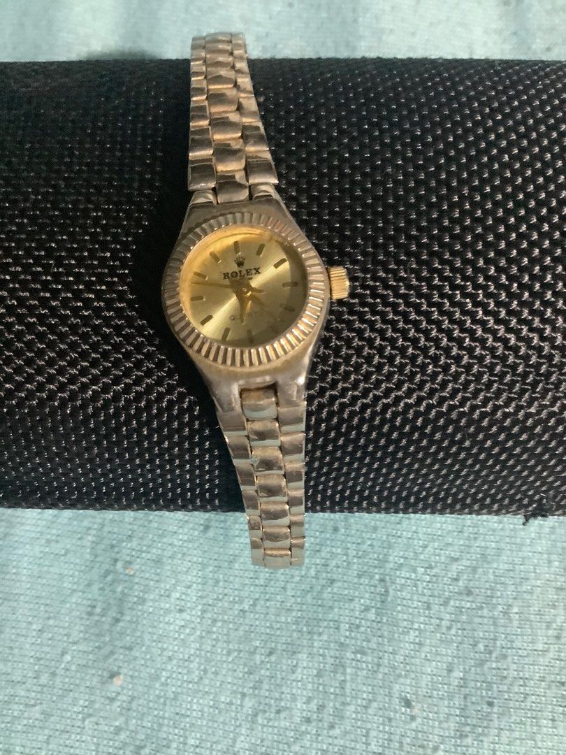 Rolex Quartz Watch (Category: Luxury Watches) located in Baguio. Submitted by agozun61 (Listing ID 1404687420, Image 1). Description: Watch features a gold-toned dial with the Rolex logo. It has a silver-toned metal strap and a fluted bezel. The back of the watch indicates it is Swiss made, water resistant, and uses a 11.60x3.10 battery. The watch has a small, round face and a crown on the side..