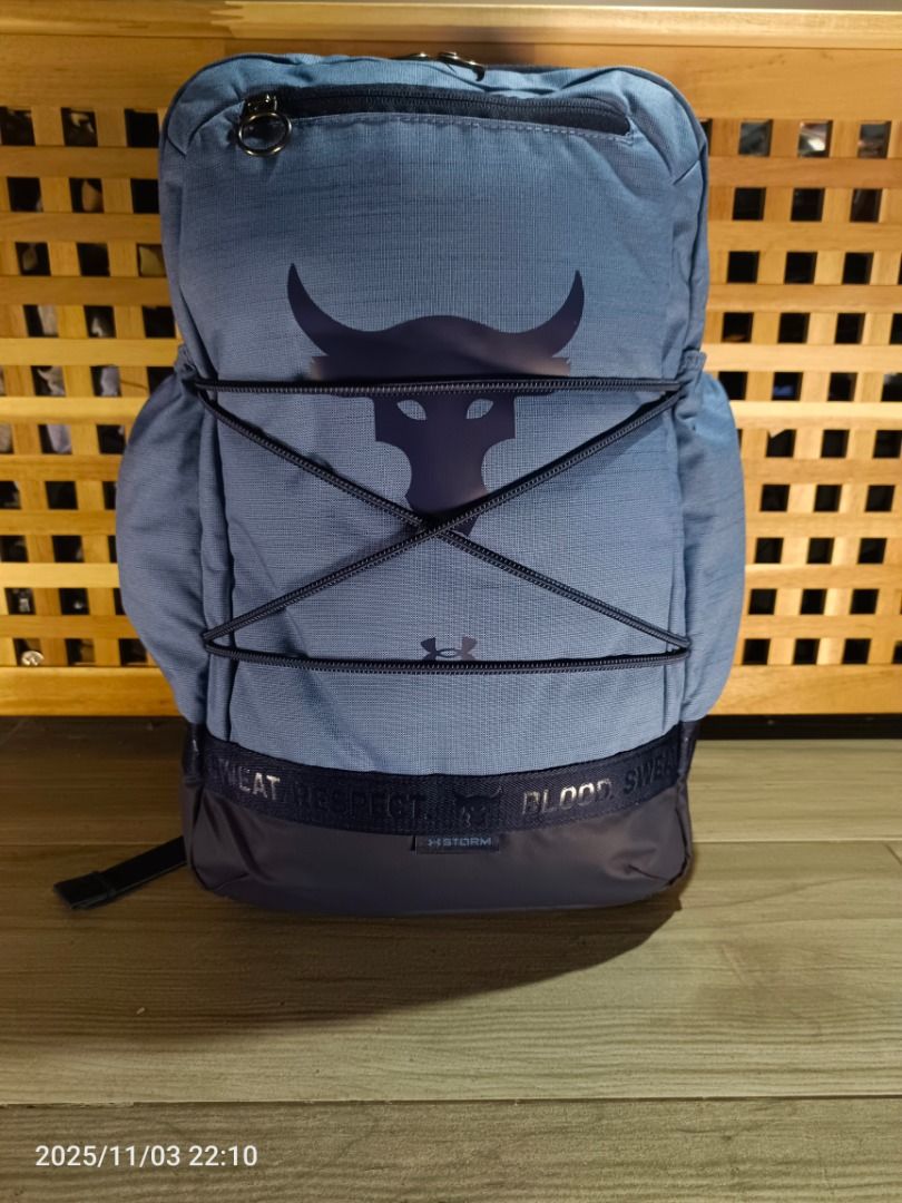Under Armour Project Rock Brahma Backpack ( Blue ) (Category: Backpacks) located in Bacoor. Submitted by the.full.cart (Listing ID 1404720667, Image 1). Description: Under Armour Project Rock backpack features a blue design with the Project Rock logo. It has multiple compartments, including a top zip pocket and side pockets. The backpack includes adjustable straps and a top handle. The front of the bag has a bungee cord system. The bottom of the 