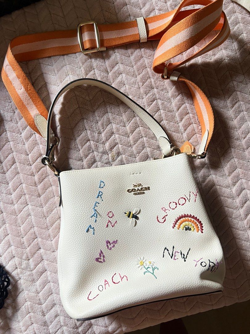Coach Embroidered Bucket Bag with Striped Strap (Category: Luxury Bags & Wallets) located in Taguig. Submitted by laurenceapo (Listing ID 1404803923, Image 1). Description: - Coach bucket bag - Embroidered details - Detachable orange and white striped strap - Top handle - Coach logo - Embroidered designs: "dream", "groovy", "new york", bee, rainbow, flowers, and butterflies - still nego.