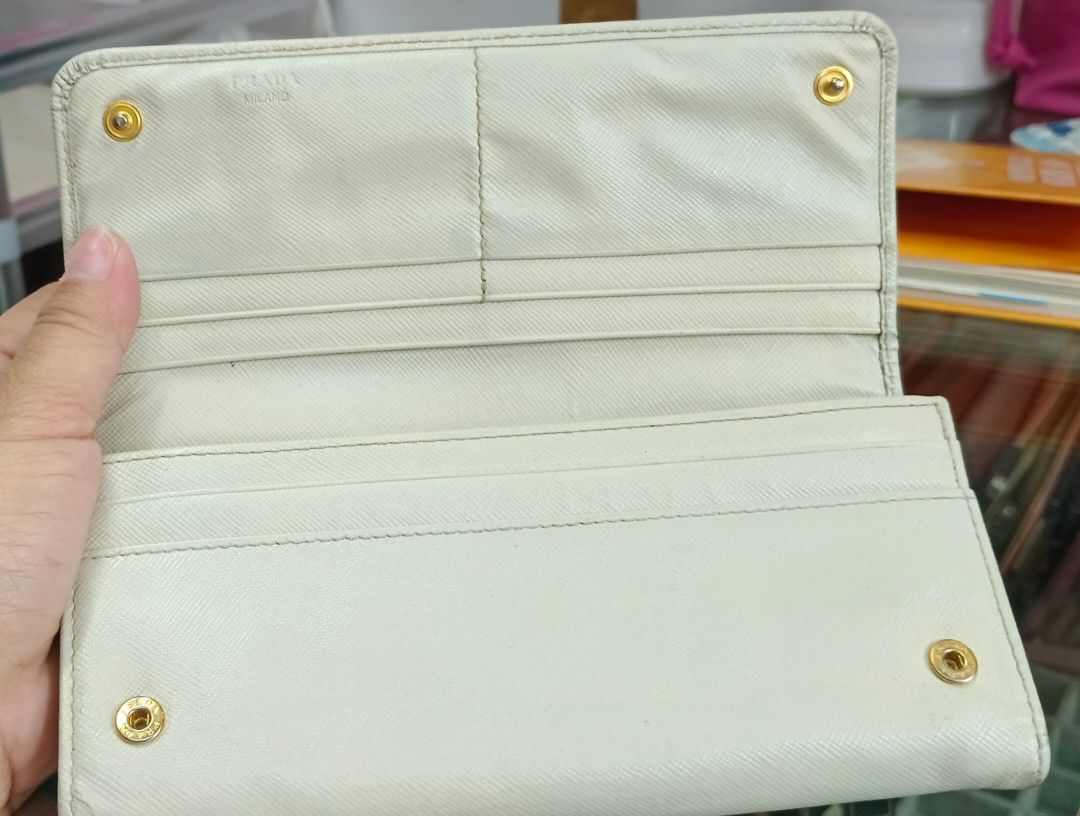 Prada Long Wallet (Category: Luxury Bags & Wallets) located in Legazpi City. Submitted by georgepineda791 (Listing ID 1401717114, Image 2). Description: Preloved Prada Long Wallet in light cream color. Features two-button lock with Prada engraving, multiple card slots, coin slot, etiketa, and code inside. Flaws: rubs on edges and body, fading hardware, tiny cracks on edges, yellowish glue stain inside pocket, and dirt/stain on the side part (poss