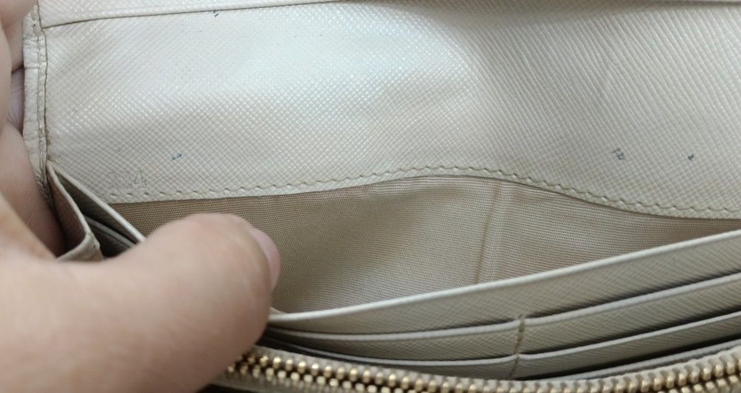 Prada Long Wallet (Category: Luxury Bags & Wallets) located in Legazpi City. Submitted by georgepineda791 (Listing ID 1401717114, Image 3). Description: Preloved Prada Long Wallet in light cream color. Features two-button lock with Prada engraving, multiple card slots, coin slot, etiketa, and code inside. Flaws: rubs on edges and body, fading hardware, tiny cracks on edges, yellowish glue stain inside pocket, and dirt/stain on the side part (poss