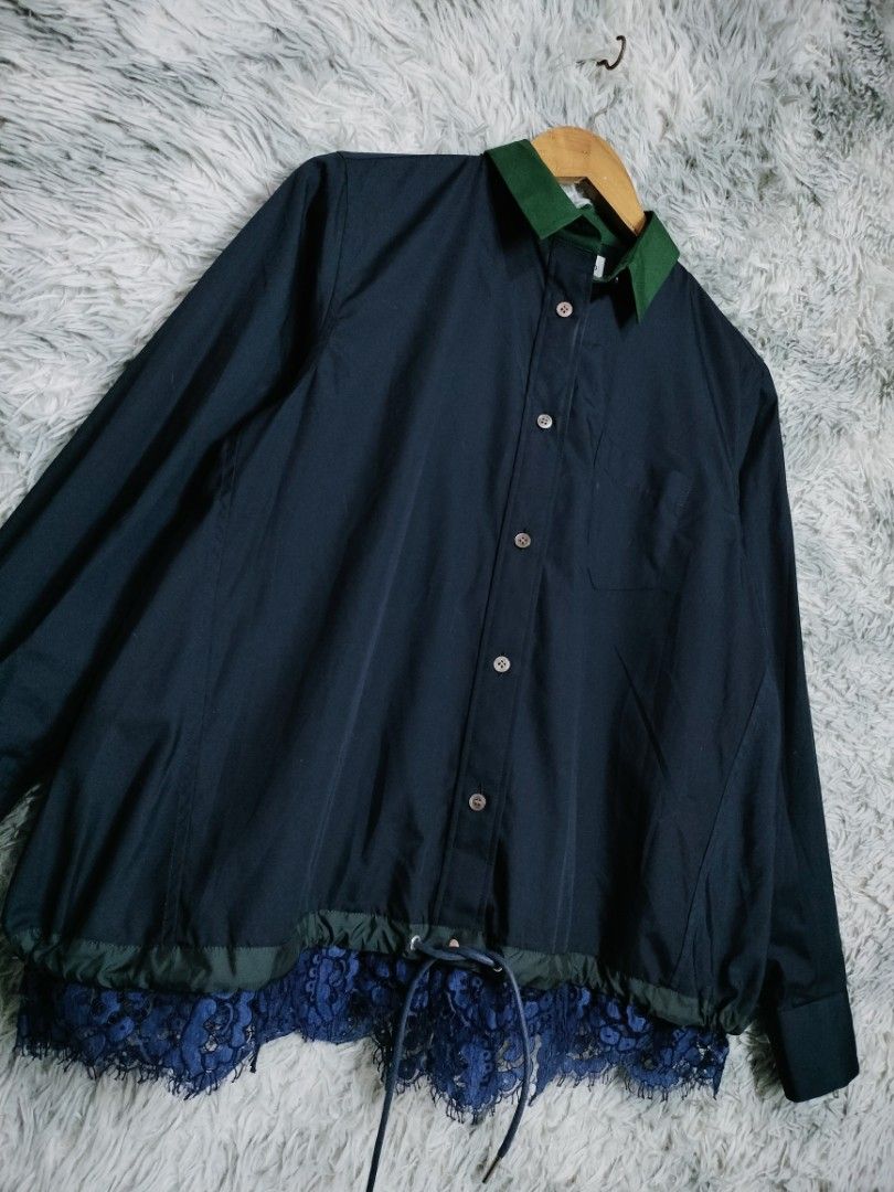 Sacai lace trim blouse navy (Category: Luxury Apparel) located in Rosales. Submitted by simplebyx.ph (Listing ID 1401850150, Image 3). Description: Navy shirt from Sacai with a green collar and lace detailing at the hem. Features a button-down front, a chest pocket, and long sleeves. The shirt has a drawstring at the waist. The tag indicates the shirt is made in Japan with a blend of polyester, cotton, rayon, and nylon. Sacai lace trim blouse nav