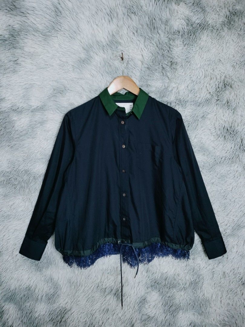 Sacai lace trim blouse navy (Category: Luxury Apparel) located in Rosales. Submitted by simplebyx.ph (Listing ID 1401850150, Image 2). Description: Navy shirt from Sacai with a green collar and lace detailing at the hem. Features a button-down front, a chest pocket, and long sleeves. The shirt has a drawstring at the waist. The tag indicates the shirt is made in Japan with a blend of polyester, cotton, rayon, and nylon. Sacai lace trim blouse nav