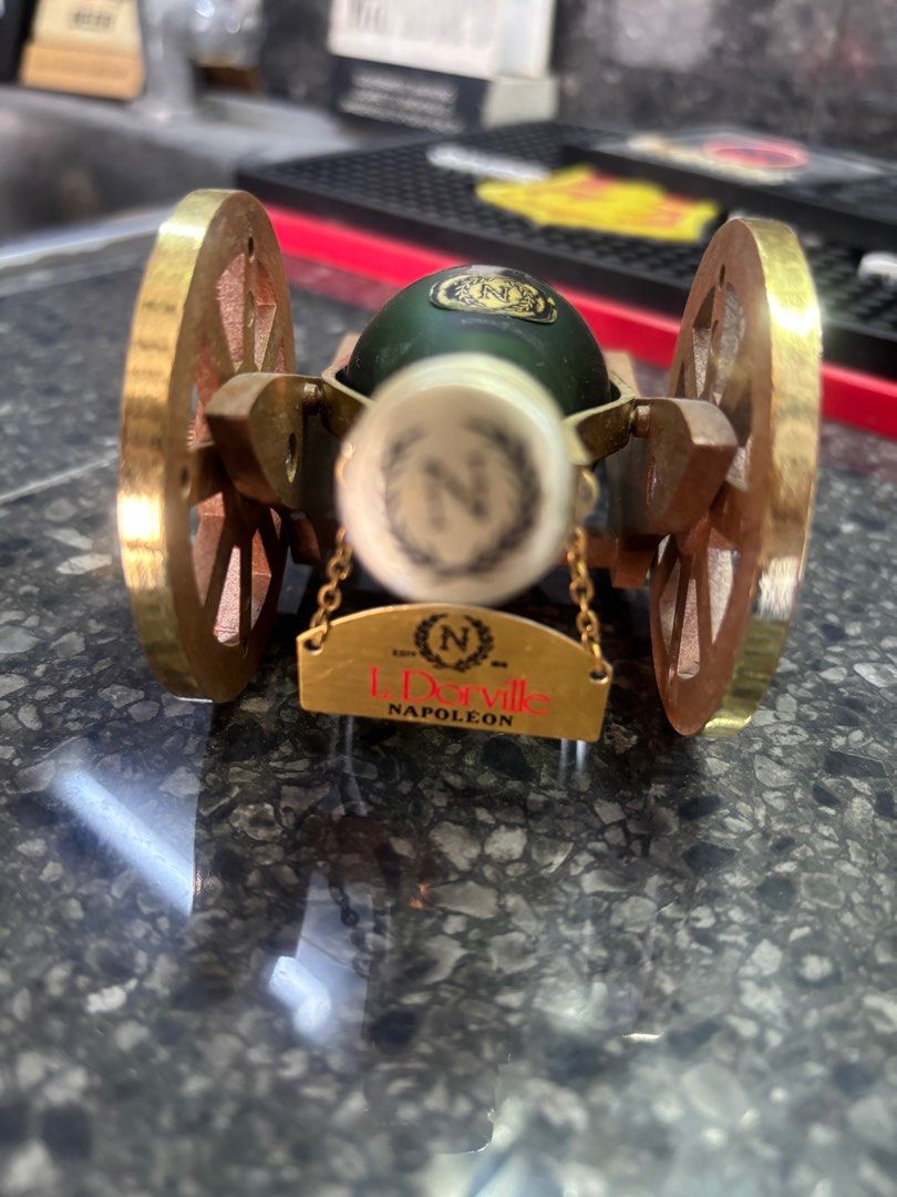 Dorville cannon mini liquor (Category: Vintage Collectibles) located in Manila. Submitted by jojopherna60447 (Listing ID 1405344356, Image 2). Description: - Miniature L. Dorville Napoleon cognac bottle. - Presented in a decorative cannon-shaped holder. - Bottle: Green glass with a gold label. - Cannon: Made of wood and brass. - Features detailed wheels and accents. - Bottle is secured within the cannon. - Label indicates 'Pure Grape Brandy'..