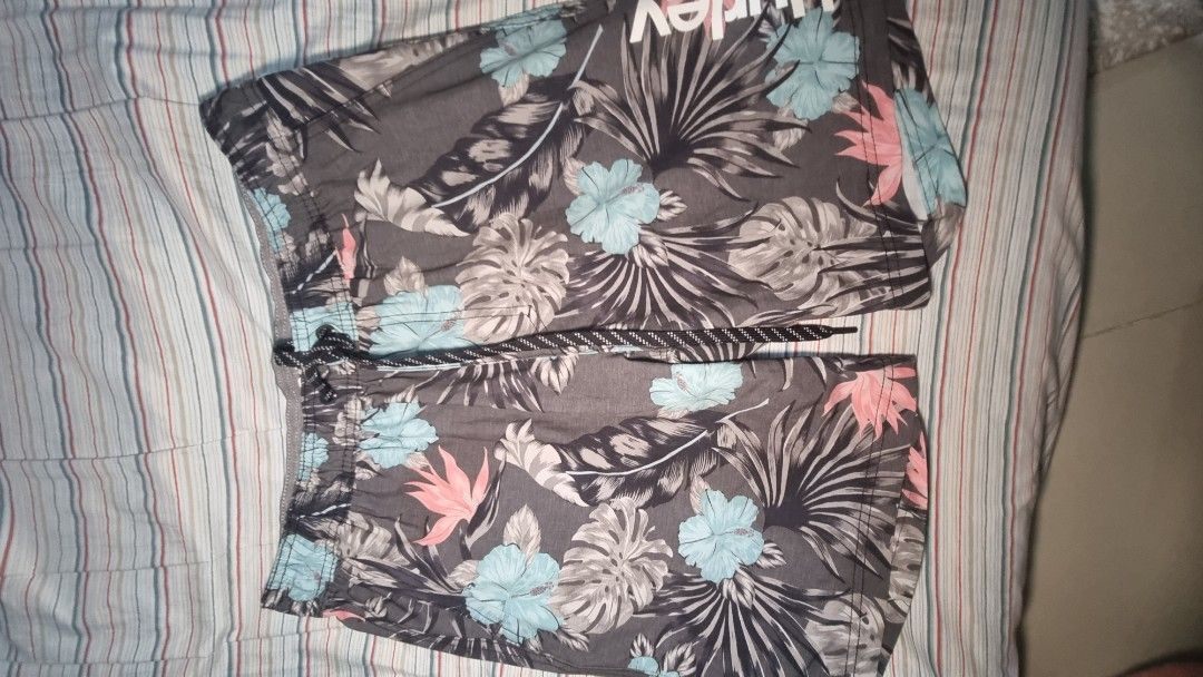 Hurley Print Board Shorts (Category: Shorts) located in Manila. Submitted by blizzardstan (Listing ID 1405187383, Image 2). Description: - Hurley floral print shorts - Dark grey base color - Features blue, pink, and white floral accents - Drawstring closure for adjustable fit - Comfortable inner lining - Hurley logo on waistband and side.