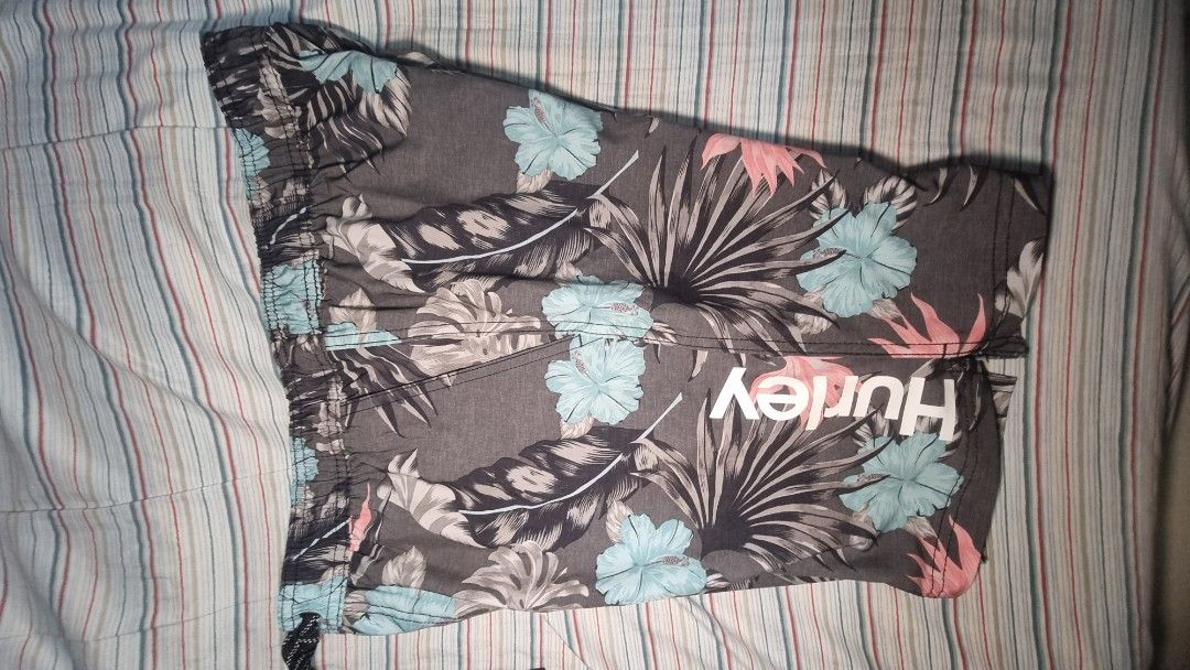 Hurley Print Board Shorts (Category: Shorts) located in Manila. Submitted by blizzardstan (Listing ID 1405187383, Image 1). Description: - Hurley floral print shorts - Dark grey base color - Features blue, pink, and white floral accents - Drawstring closure for adjustable fit - Comfortable inner lining - Hurley logo on waistband and side.