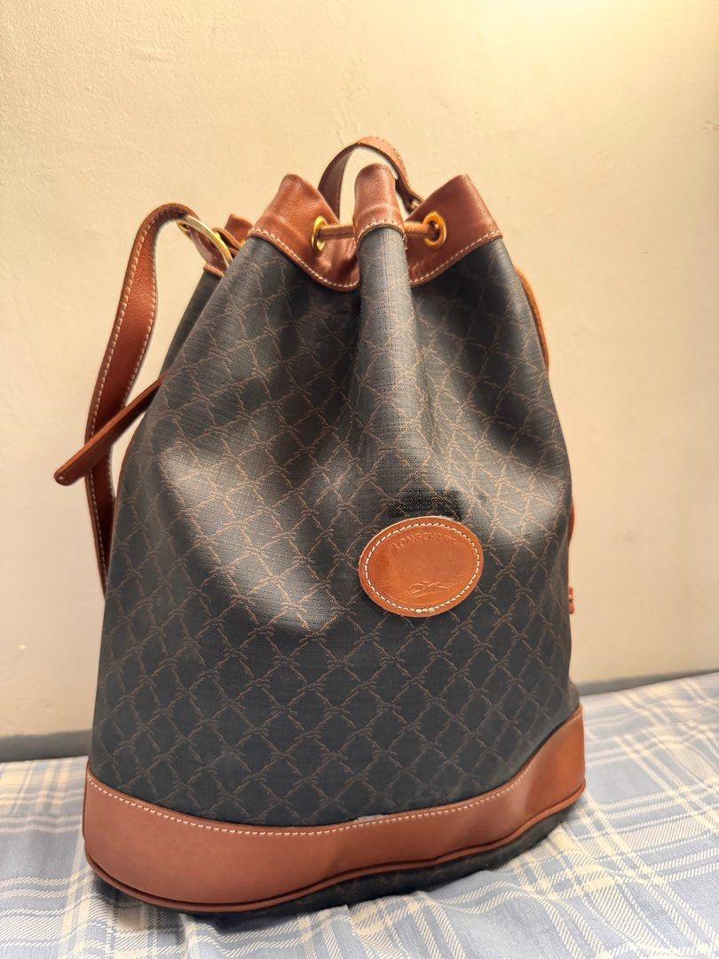 Longchamp Vintage Leather Bucket Bag (Category: Luxury Bags & Wallets) located in Rosales. Submitted by thriftingismygame (Listing ID 1405217703, Image 2). Description: - Vintage Longchamp bucket bag - Brown leather trim and strap - Drawstring closure - Brown patterned exterior - Features Longchamp logo patch - Beige interior with zipper pocket - Made in France Some few signs of usage.