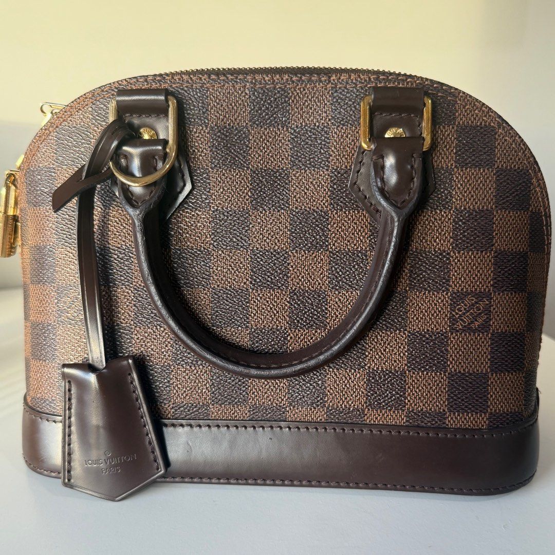Louis Vuitton Alma BB Damier Ebene (Category: Luxury Bags & Wallets) located in Taguig. Submitted by nicolefits_ (Listing ID 1405249618, Image 3). Description: - Authentic Louis Vuitton Alma BB handbag - Damier Ebene canvas - Top zip closure - Rolled leather handles - Detachable shoulder strap - Includes padlock and keys with clochette - Red fabric interior with pocket - Elegant gold-tone hardware.