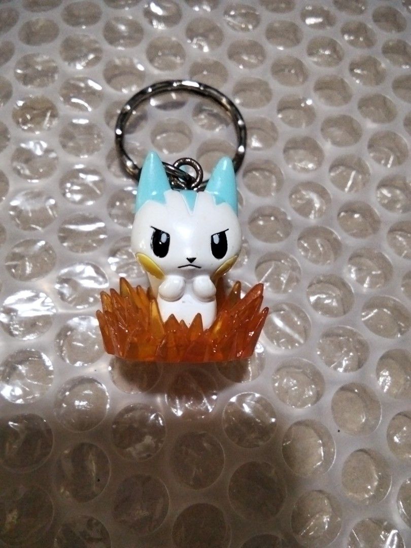 Anime Character Keychain (Category: Character Goods) located in Santa Rosa. Submitted by animemerchcollection (Listing ID 1405560350, Image 1). Description: - Adorable anime character keychain - Features a white body with blue accents - Includes a yellow cheek detail - Character design: Sitting in orange flames - Comes with a durable silver keyring.