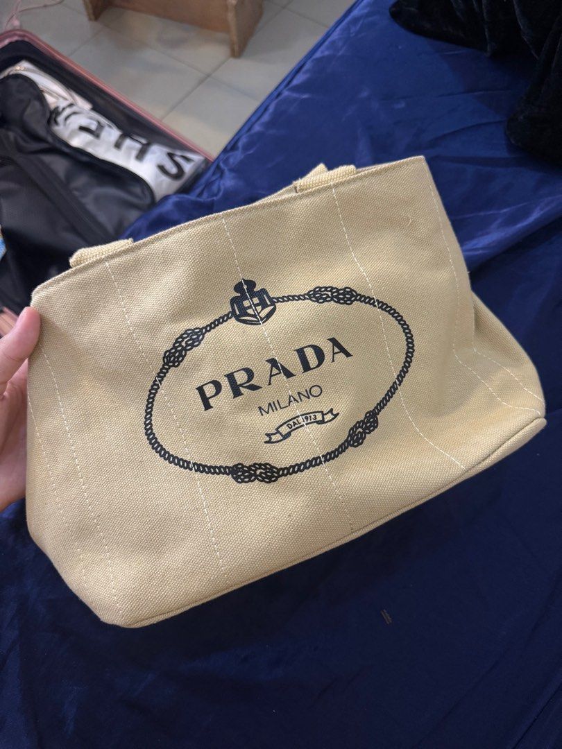 Prada Canvas Tote Bag (Category: Luxury Bags & Wallets) located in Manila. Submitted by lexie.xoxo (Listing ID 1405654231, Image 1). Description: - Authentic Prada tote bag - Features the iconic Prada logo - Beige canvas exterior with vertical stripe detailing - Two handles for carrying - Classic design - Ideal for everyday use.