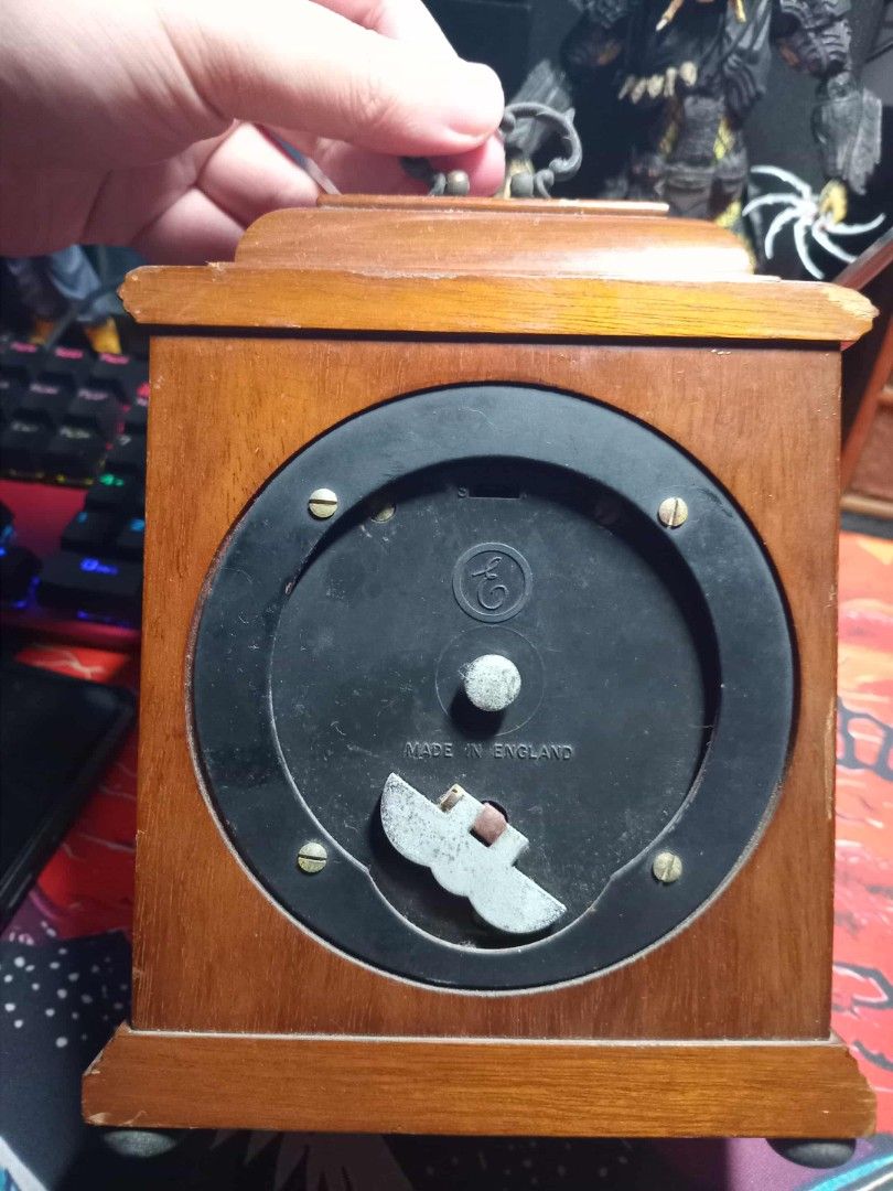 Vintage Wooden Elliot Clock (Category: Clocks) located in Taguig. Submitted by ashicollection (Listing ID 1405707292, Image 2). Description: - Vintage wooden clock - Gold-colored clock face with Roman numerals - Wooden frame - Winding mechanism marked "Made in England" - Features a handle - Decorative elements on clock face.