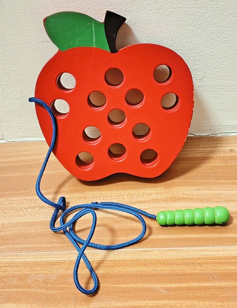 Wooden Apple Lacing Toy (Category: Educational & Learning Toys) located in Tanza. Submitted by c.avel (Listing ID 1405825348, Image 1). Description: Wooden lacing toy features a red apple shape with holes for lacing. It includes a blue string with a green caterpillar-shaped end. The toy is designed to help children develop fine motor skills and hand-eye coordination. The apple has a green leaf and a black stem. The toy is made of wood..