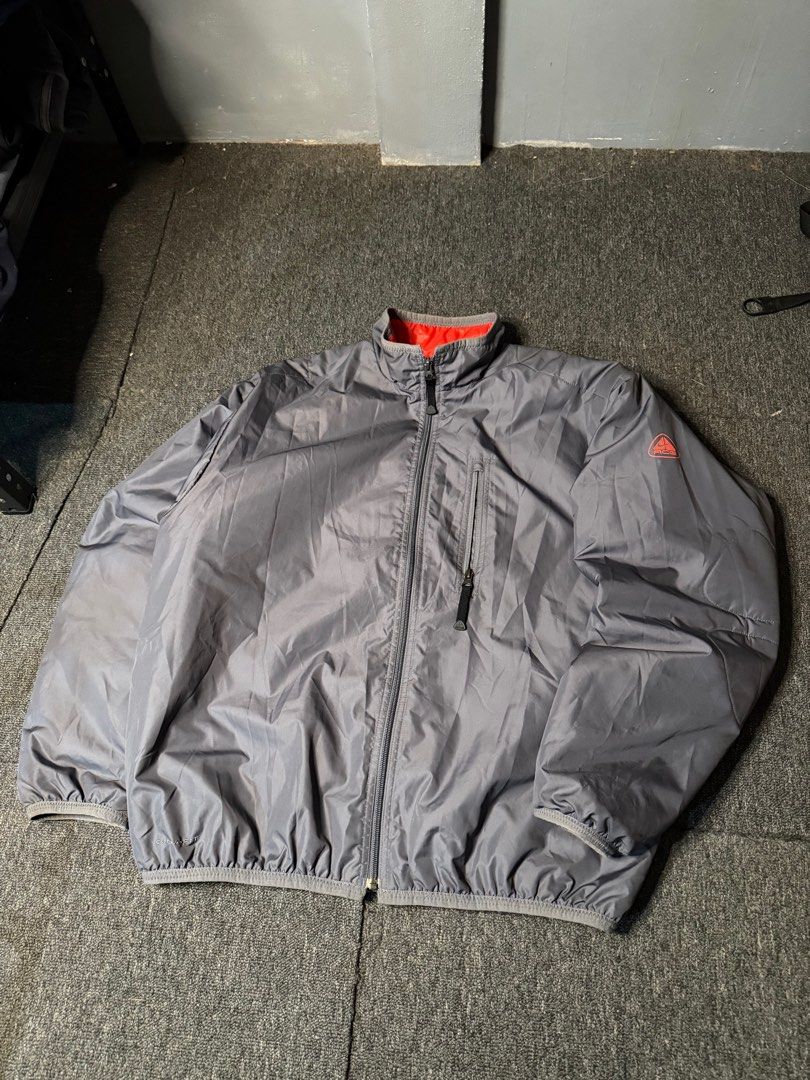 Nike ACG Puffer Windbreaker (Category: Coats, Jackets and Outerwear) located in San Marcelino. Submitted by SoloMain (Listing ID 1406055118, Image 2). Description: Nike ACG puffer windbreaker features a gray exterior with a red interior. It has a zip closure, a pocket on the chest, and the ACG logo on the sleeve. The jacket is labeled as Clima-Fit. The width is 25.5 inches and the length is 27.5 inches..