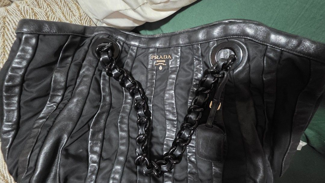 Prada Black Chain Tote Bag (Category: Luxury Bags & Wallets) located in Mandaluyong City. Submitted by snapitupgoods (Listing ID 1406015862, Image 1). Description: Black Prada tote bag with chain straps. Features a pleated design and a Prada logo on the front. The interior has a Prada logo lining. Includes a small leather tag attached to the chain. The bag has a zipper closure..