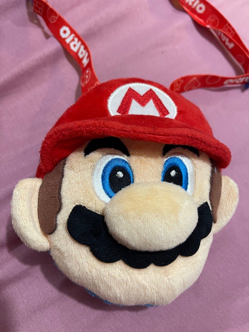 Super Nintendo World Mario Plush Shoulder Pouch (Category: Plushies & Soft Toys) located in Arayat. Submitted by imeon13 (Listing ID 1406082860, Image 2). Description: Adorable Mario plush shoulder pouch is from Super Nintendo World at Universal Studios Japan. It features a red cap with the iconic "M" logo, a blue body, and a red zipper. The interior is orange with star patterns. The pouch comes with a red Mario-themed lanyard. Perfect for carryi