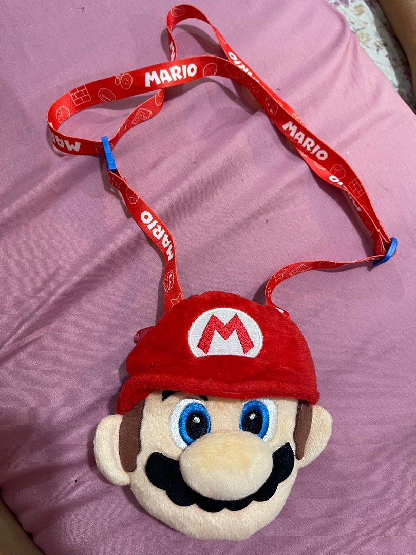 Super Nintendo World Mario Plush Shoulder Pouch (Category: Plushies & Soft Toys) located in Arayat. Submitted by imeon13 (Listing ID 1406082860, Image 1). Description: Adorable Mario plush shoulder pouch is from Super Nintendo World at Universal Studios Japan. It features a red cap with the iconic "M" logo, a blue body, and a red zipper. The interior is orange with star patterns. The pouch comes with a red Mario-themed lanyard. Perfect for carryi