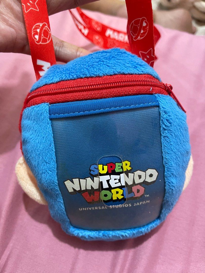 Super Nintendo World Mario Plush Shoulder Pouch (Category: Plushies & Soft Toys) located in Arayat. Submitted by imeon13 (Listing ID 1406082860, Image 3). Description: Adorable Mario plush shoulder pouch is from Super Nintendo World at Universal Studios Japan. It features a red cap with the iconic "M" logo, a blue body, and a red zipper. The interior is orange with star patterns. The pouch comes with a red Mario-themed lanyard. Perfect for carryi