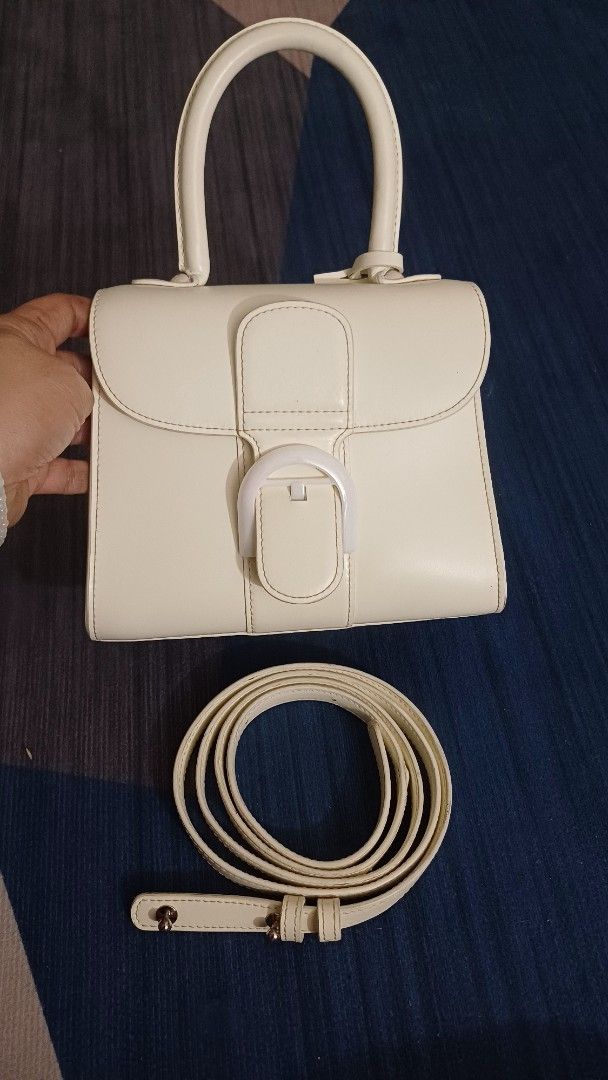 Delvaux Ivory Handbag with Strap (Category: Luxury Bags & Wallets) located in Lemery. Submitted by venus23 (Listing ID 1406281768, Image 1). Description: - Delvaux ivory handbag - Detachable shoulder strap included - Features a top handle - Secure buckle closure - Multiple interior compartments - Structured, rectangular design - Brand: Delvaux.
