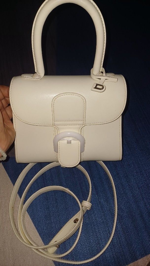 Delvaux Ivory Handbag with Strap (Category: Luxury Bags & Wallets) located in Lemery. Submitted by venus23 (Listing ID 1406281768, Image 2). Description: - Delvaux ivory handbag - Detachable shoulder strap included - Features a top handle - Secure buckle closure - Multiple interior compartments - Structured, rectangular design - Brand: Delvaux.