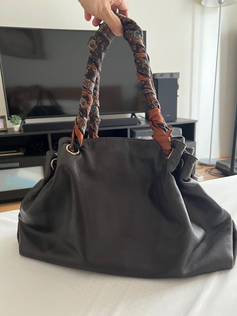 MUST GO!! FURLA Leather Handbag (Category: Luxury Bags & Wallets) located in Las Pinas. Submitted by sabs28 (Listing ID 1406158113, Image 1). Description: - Authentic Furla leather handbag - Dark brown exterior - Spacious interior with zippered and small pockets - Wrapped with a patterned scarf due to some tears in handles - Metal feet on the bottom - Furla logo visible inside and outside.