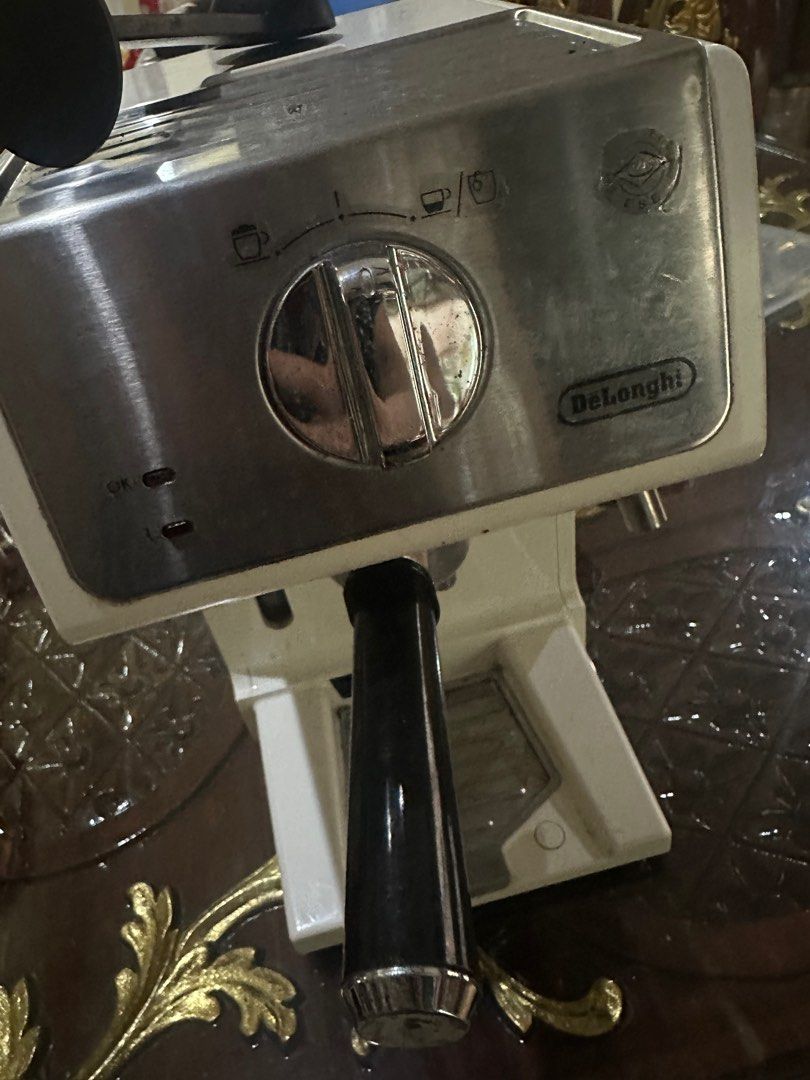 DeLonghi Espresso Machine (Category: Coffee Machines & Makers) located in Quezon City. Submitted by luxmamaqc (Listing ID 1406346340, Image 1). Description: DeLonghi espresso machine with a stainless steel and white finish. Features a steam wand and a dial for different coffee settings. Includes a portafilter holder. The power cord is included. The machine has a few signs of use..