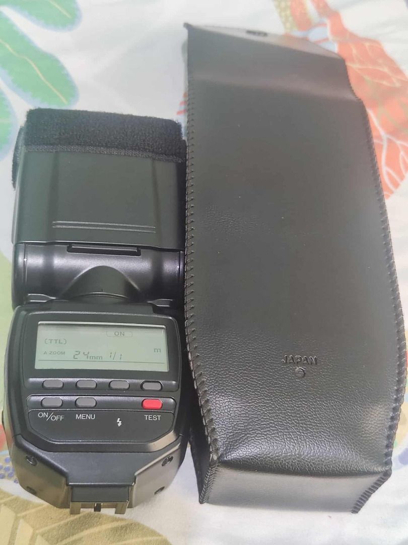 Minolta Program 5200i Flash (working) (Category: Cameras) located in Manila. Submitted by butihingmakinarya (Listing ID 1406330479, Image 1). Description: Minolta Program 5200i flash unit. Includes the flash unit and a protective case. The flash has an LCD screen displaying settings. The flash is turned on and set to TTL mode. The flash head has a zoom function. The battery compartment is visible..