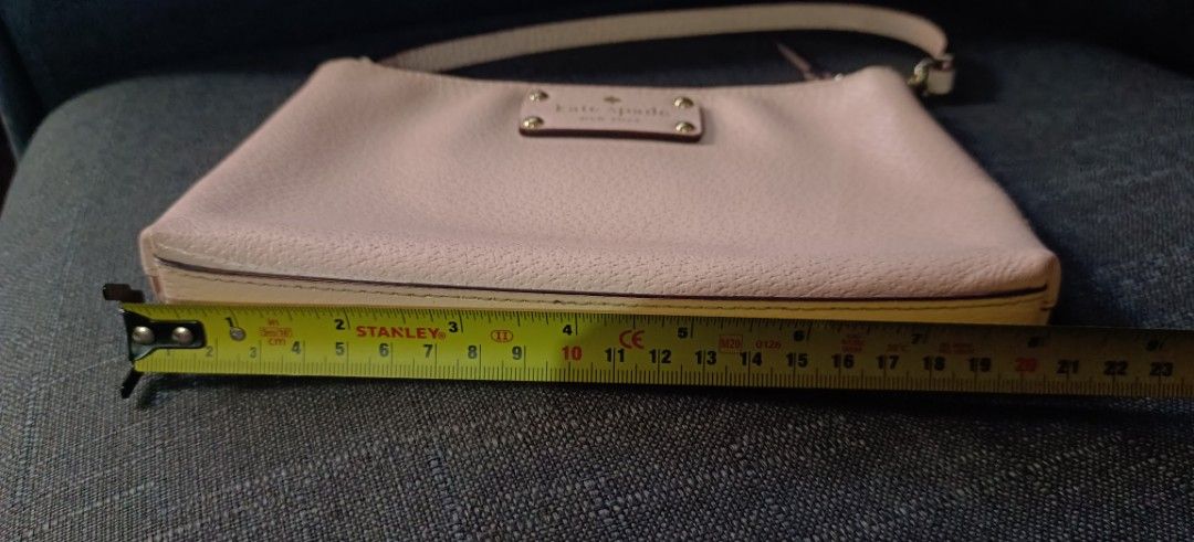 Kate Spade New York Handbag (Category: Luxury Bags & Wallets) located in Muntinlupa City. Submitted by amara211629 (Listing ID 1406712374, Image 2). Description: Kate Spade handbag features a light pink exterior with a top handle and a zipper closure. The interior has a fabric lining with the Kate Spade New York logo. The bag has a small rectangular shape. The bag measures approximately 20cm in length and 13cm in height. It has a detachable strap
