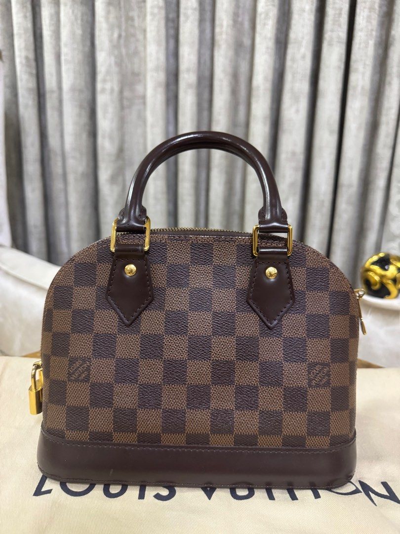 Louis Vuitton Alma BB Damier Ebene Authentic (Category: Luxury Bags & Wallets) located in Makati City. Submitted by happyprelovedph (Listing ID 1406856228, Image 2). Description: - Louis Vuitton Alma BB handbag - Iconic Damier Ebene canvas - Top handle - Secure zip closure - Gold-tone hardware - Brown leather base - Red fabric interior - Includes leather clochette and tag - Lost Sling.