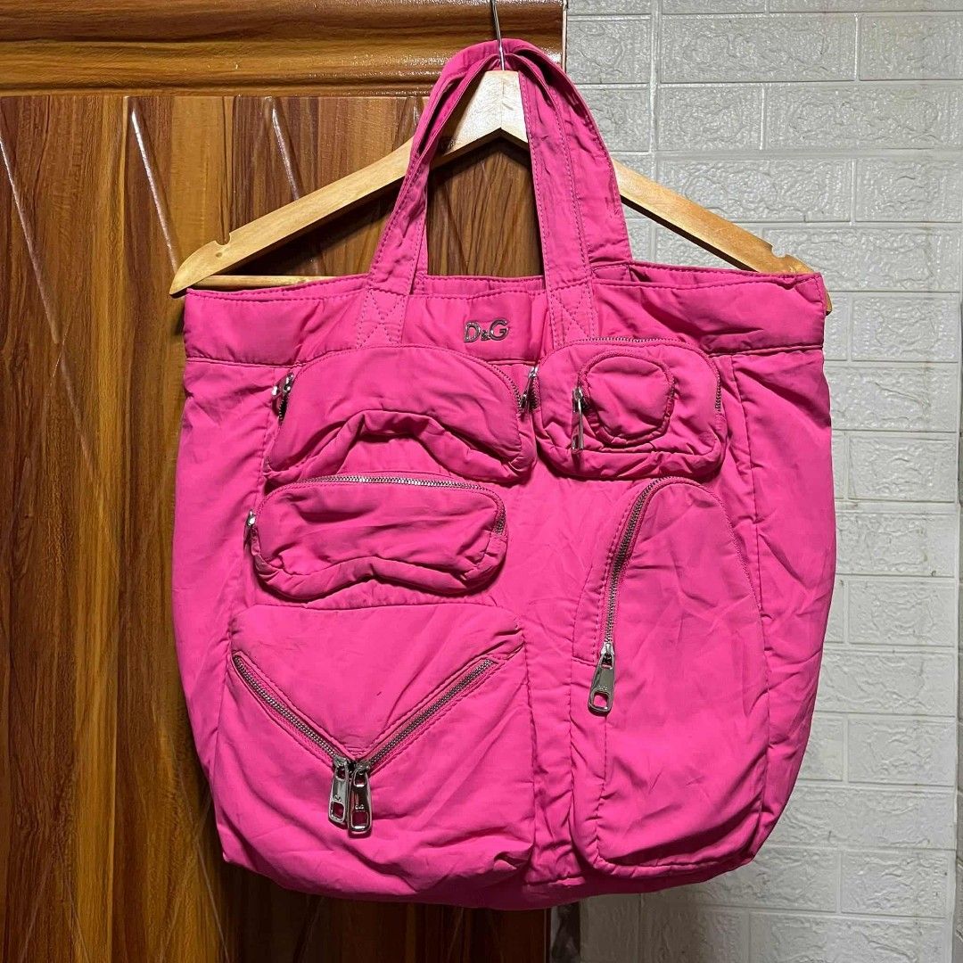 D&G Pink Tote Bag (Category: Luxury Bags & Wallets) located in Carmen. Submitted by ar_thrift00 (Listing ID 1401915539, Image 1). Description: D&G tote bag features a vibrant pink color and multiple exterior pockets with zipper closures. The interior includes a zippered pocket and a brand label. The bag has two top handles for carrying. The D&G logo is visible on the front of the bag..
