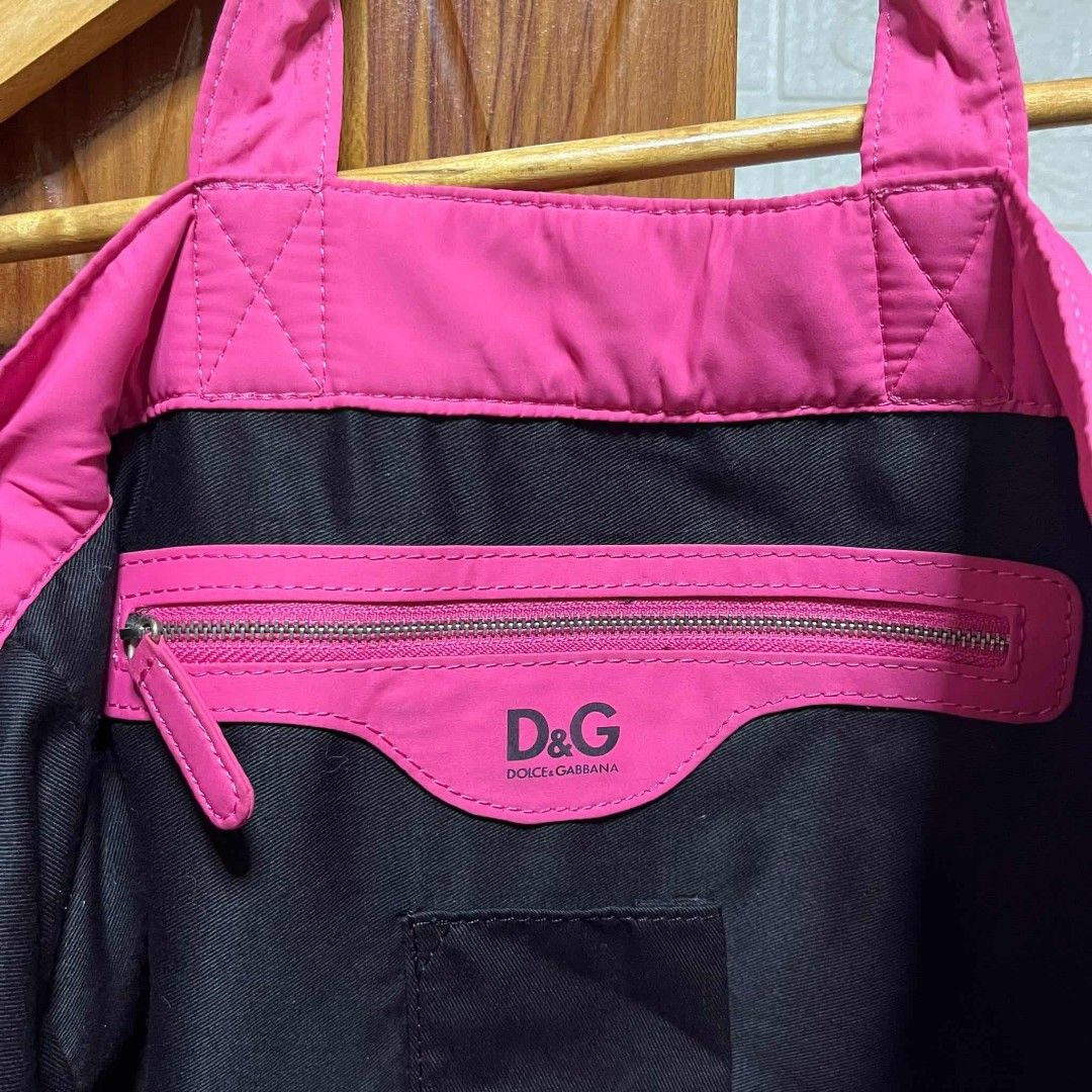 D&G Pink Tote Bag (Category: Luxury Bags & Wallets) located in Carmen. Submitted by ar_thrift00 (Listing ID 1401915539, Image 2). Description: D&G tote bag features a vibrant pink color and multiple exterior pockets with zipper closures. The interior includes a zippered pocket and a brand label. The bag has two top handles for carrying. The D&G logo is visible on the front of the bag..