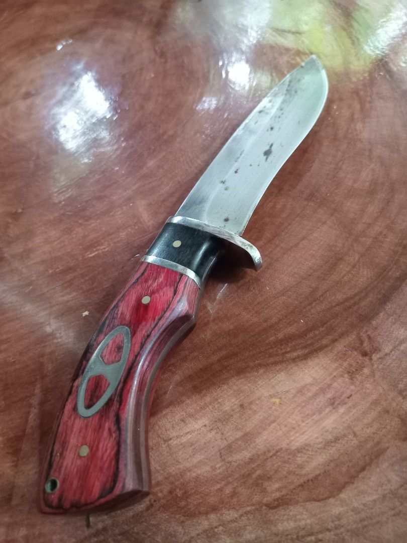 Hunting Knife with Sheath (Category: Knives & Chopping Boards) located in Atimonan. Submitted by russ.rizz (Listing ID 1401945647, Image 1). Description: - Stainless steel blade - Red and black wooden handle - Includes black sheath - Decorative metal inlay on handle - Ideal for outdoor activities.