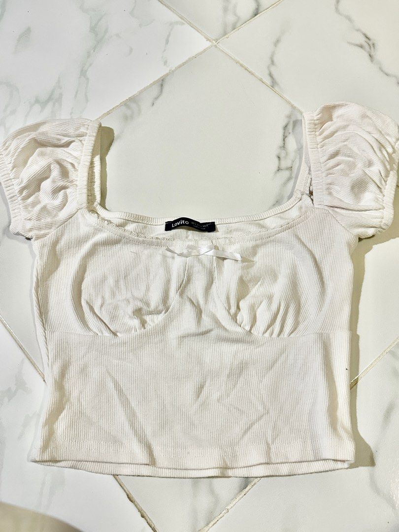 Lovito White Puff Sleeve Top (Category: Blouses) located in Manila. Submitted by cchaiprincess (Listing ID 1401948469, Image 1). Description: - Lovito white top - Puff sleeves - Square neckline - Small bow detail at bust - Ribbed texture - Fitted silhouette - Tag visible - Solid white color.