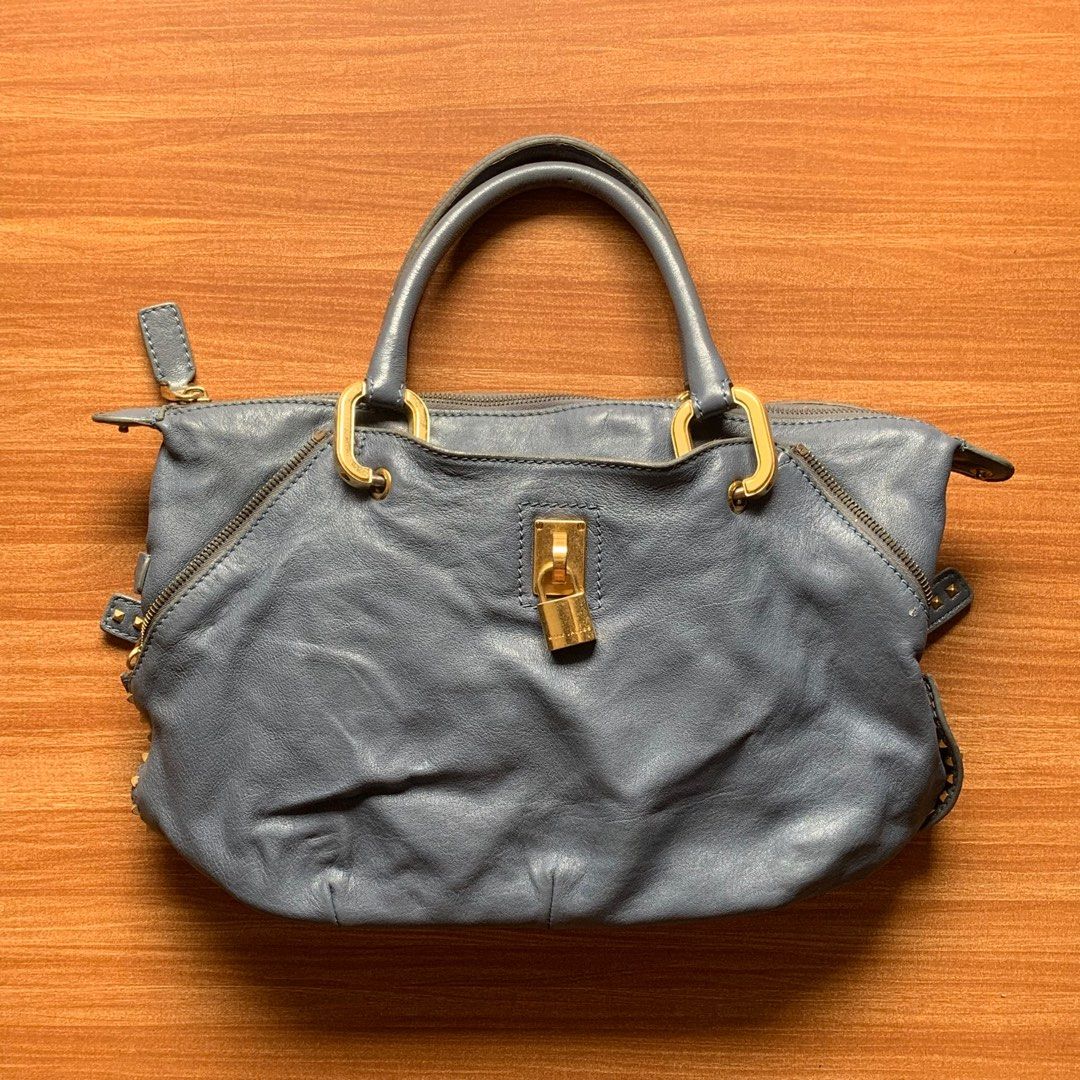 Marc Jacobs Leather Handbag (Category: Luxury Bags & Wallets) located in Cavite. Submitted by pickednthrift64 (Listing ID 1401924316, Image 1). Description: - Authentic Marc Jacobs handbag - Blue leather exterior - Gold-tone hardware - Top handle - Zip closure - Padlock detail - RIRI zipper - Visible interior lining - Some wear on handle - Spacious interior.