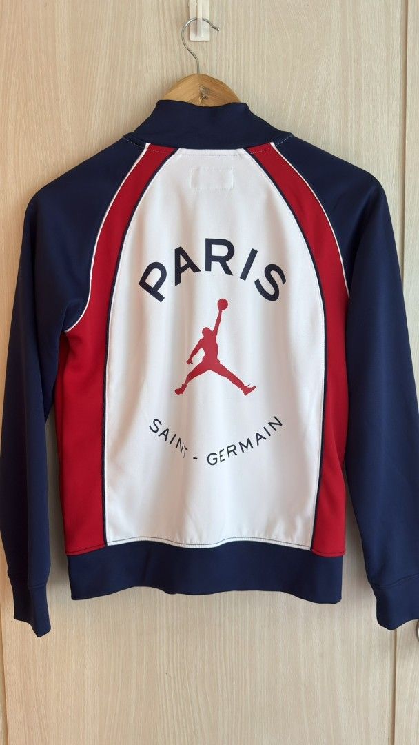 Jordan Paris Saint-Germain Track Jacket (Category: Babies & Kids Fashion) located in Makati City. Submitted by styledge.ph (Listing ID 1402185125, Image 2). Description: Jordan track jacket features the Paris Saint-Germain logo and branding. It has a full zip closure, with a white body, red side panels, and navy blue sleeves. The back displays "PARIS" and "SAINT-GERMAIN" with the Jumpman logo. The jacket is size M, suitable for 10-12 years old, F