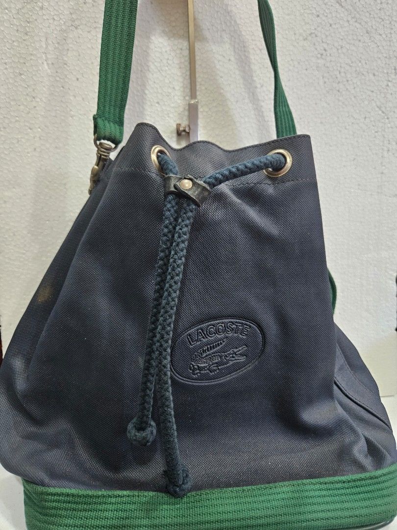 Lacoste Drawstring Bag (Category: Luxury Bags & Wallets) located in Quezon City. Submitted by bags4ever (Listing ID 1402254790, Image 1). Description: Authentic Lacoste drawstring bag. Features a navy blue exterior with green accents. Includes a drawstring closure and a shoulder strap. The interior has a zippered pocket. Made in France and Italy. The bag has a Lacoste logo patch on the front..