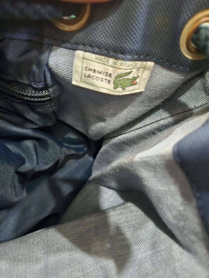 Lacoste Drawstring Bag (Category: Luxury Bags & Wallets) located in Quezon City. Submitted by bags4ever (Listing ID 1402254790, Image 3). Description: Authentic Lacoste drawstring bag. Features a navy blue exterior with green accents. Includes a drawstring closure and a shoulder strap. The interior has a zippered pocket. Made in France and Italy. The bag has a Lacoste logo patch on the front..