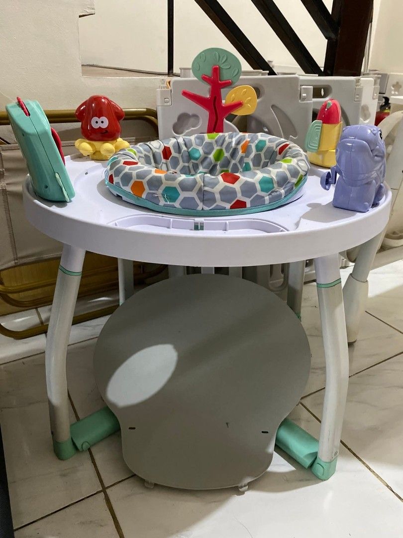 Baby Activity Center (Category: Infant Playtime) located in Manila. Submitted by justinbc89000 (Listing ID 1402293261, Image 1). Description: Baby activity center features a round table with various toys attached. It includes a seat with a colorful patterned fabric. The table has a gray seat underneath. The legs are white with green accents. There are several toys on the table, including a red octopus, a tree, and a rocket..