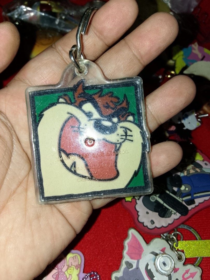 Tazmanian Devil Keychain (Category: Character Goods) located in Davao. Submitted by Ysang40 (Listing ID 1402313331, Image 2). Description: Keychain features the Tazmanian Devil character. It has a square shape with a clear plastic border. The keychain is attached to a metal ring. The design shows the Tazmanian Devil's face with a green background..