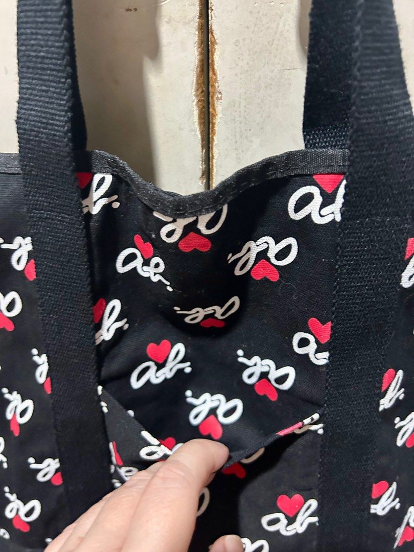 Agnes B. Voyage Tote Bag (Category: Tote Bags) located in Quezon City. Submitted by asiaco (Listing ID 1402727017, Image 2). Description: Black Agnes B. Voyage tote bag with a repeating logo and heart pattern. Features a front pocket and sturdy black handles. The bag measures approximately 38 cm in width. The interior includes a tag with Japanese text. Perfect for everyday use..